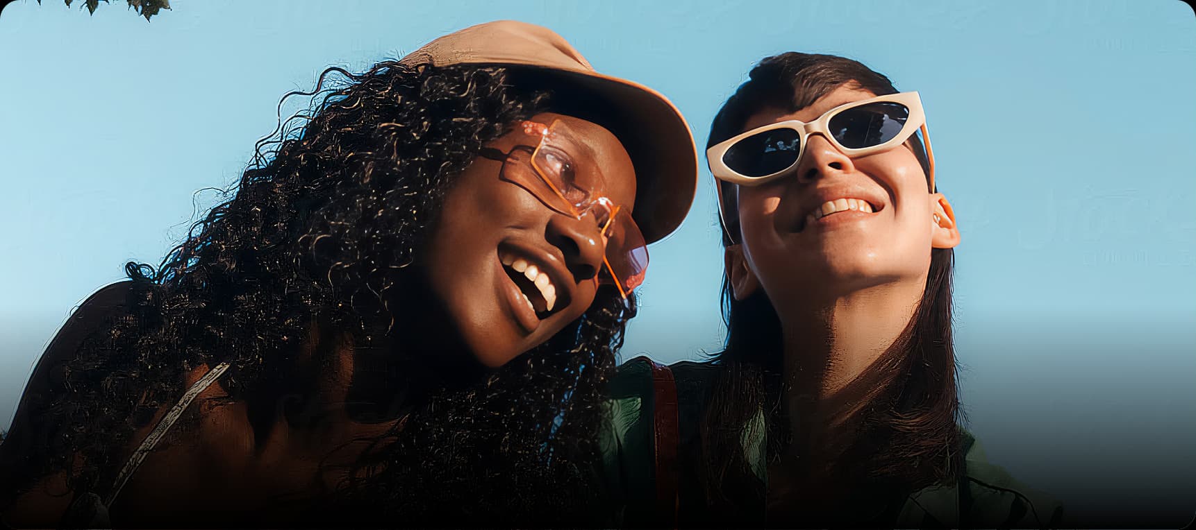 Dos mujeres jóvenes sonriendo felizmente con gafas de sol en un día soleado, representando la confianza y alegría que brinda una sonrisa saludable